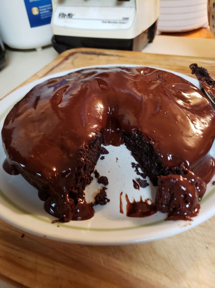 An image of a flourless chocolate cake covered with dark chocolate ganache and with a slice taken out showing how moist the cake is inside.